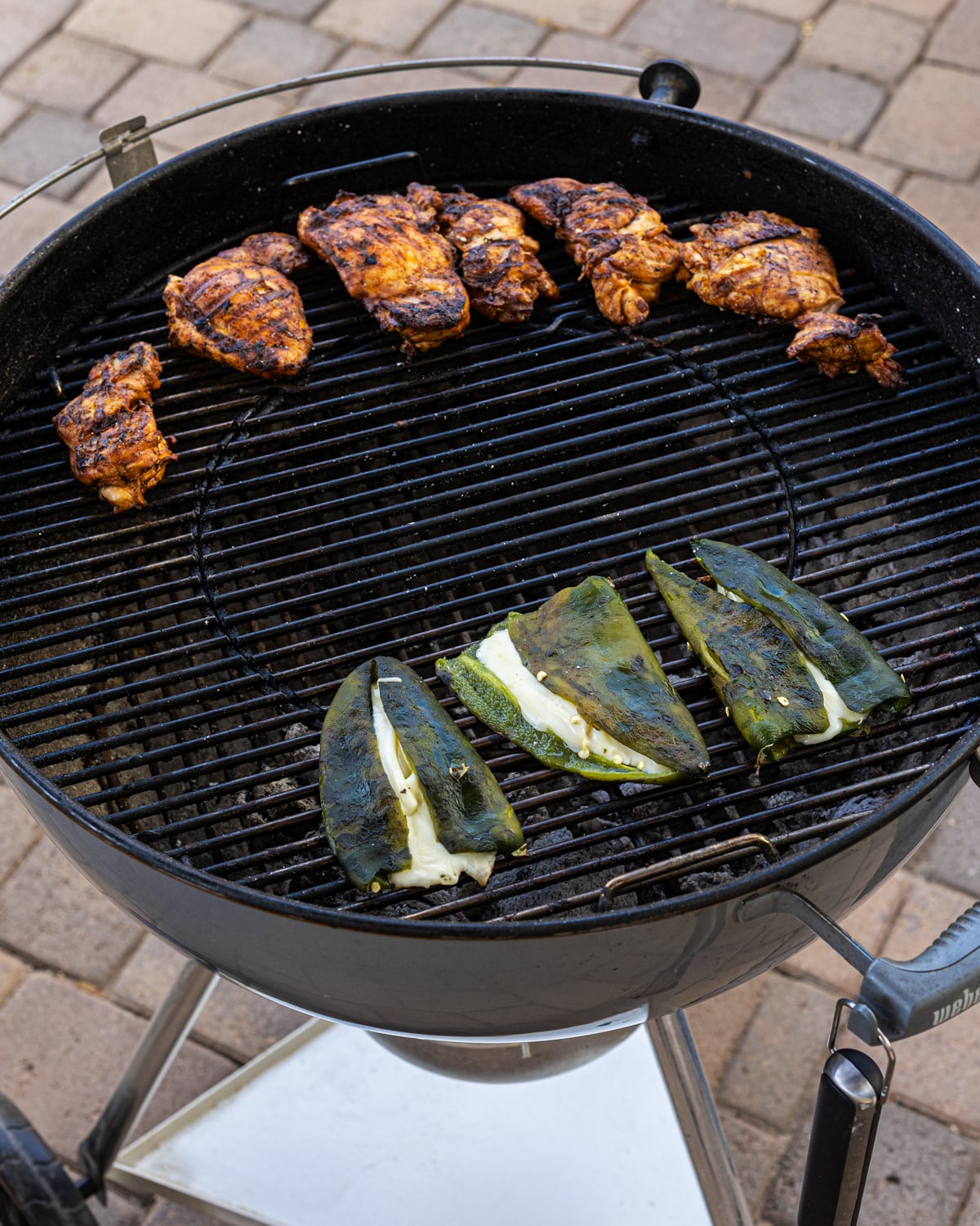 Grilled chicken thighs resting on the indirect zone while cheese-stuffed poblanos melt on the grill below