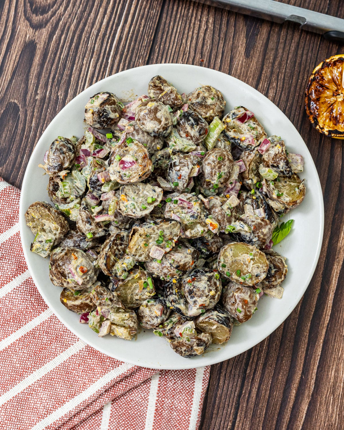 Overhead view of grilled potato salad on a white plate with chives, lemon zest, and grilled lemon half to the side