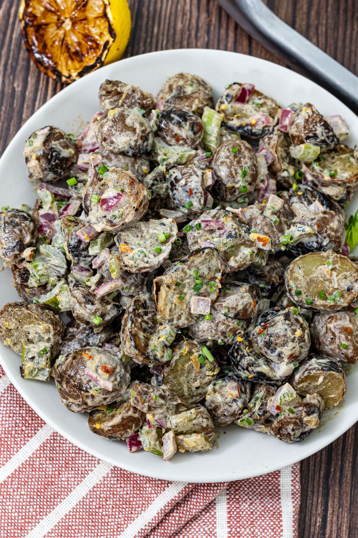 Grilled potato salad on a white plate showing charred potato skins, grilled celery and red onion, fresh chives, and lemon zest