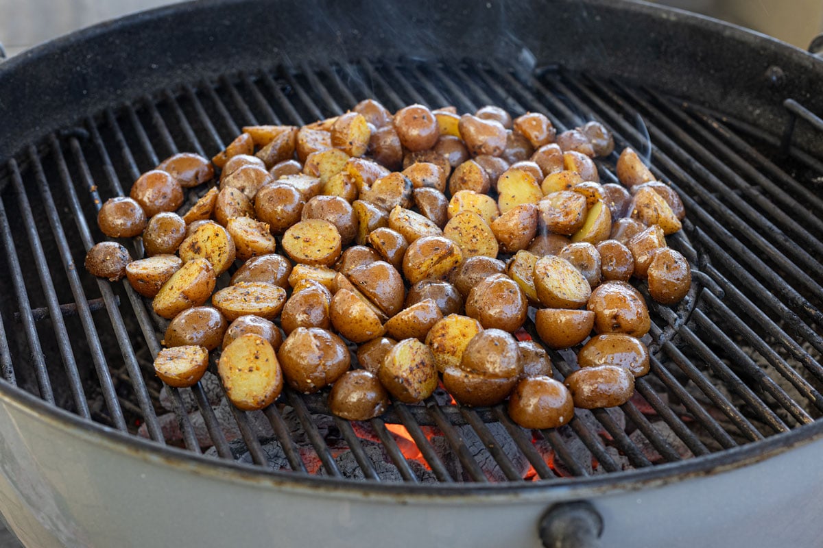 Halved mini potatoes placed cut-side down on a charcoal grill at the start of the cook