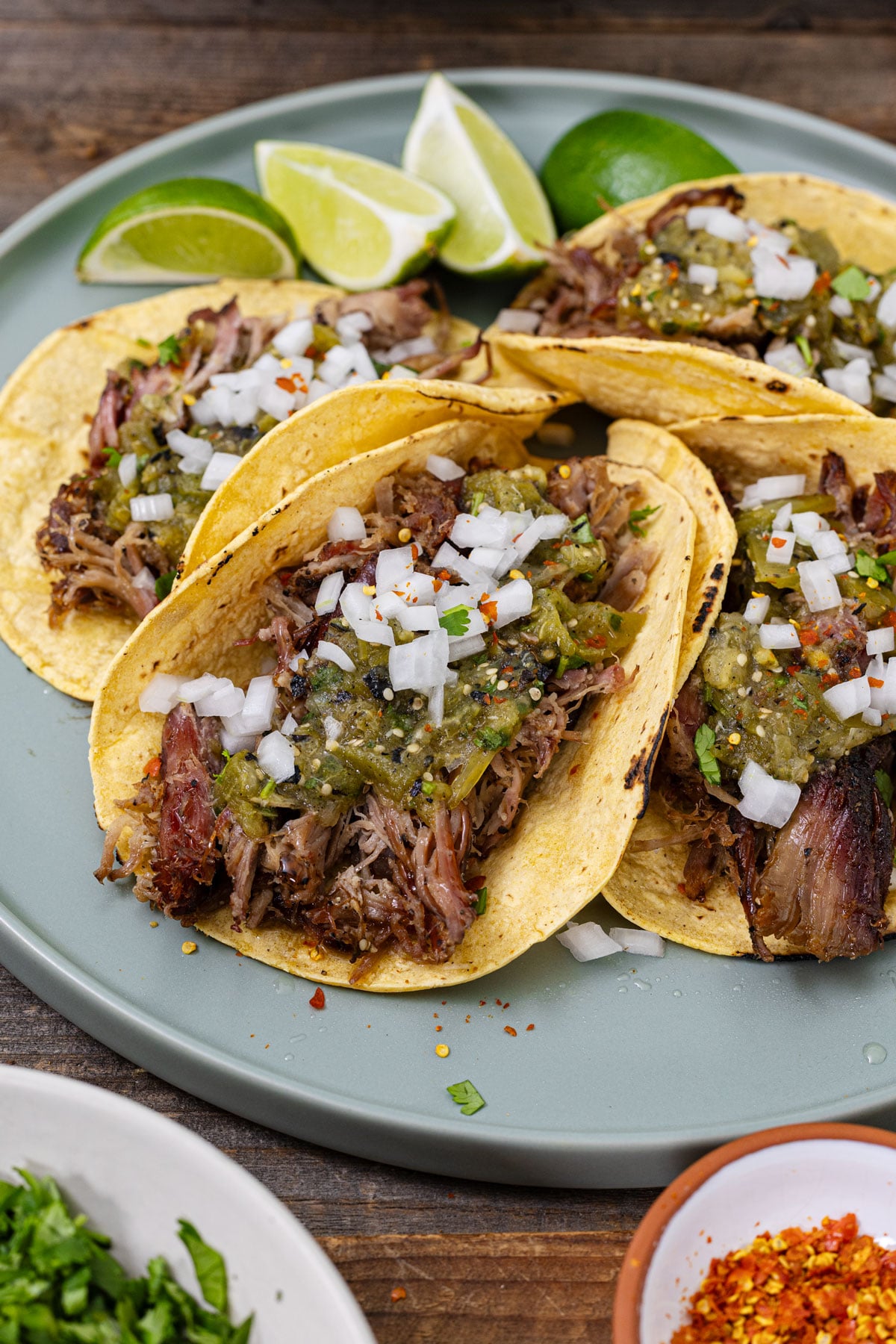 Smoked carnitas tacos on corn tortillas topped with salsa verde, diced white onion, and fresh lime