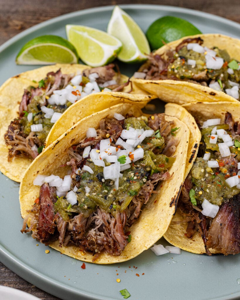 Smoked carnitas tacos with charred salsa verde and diced white onion on corn tortillas