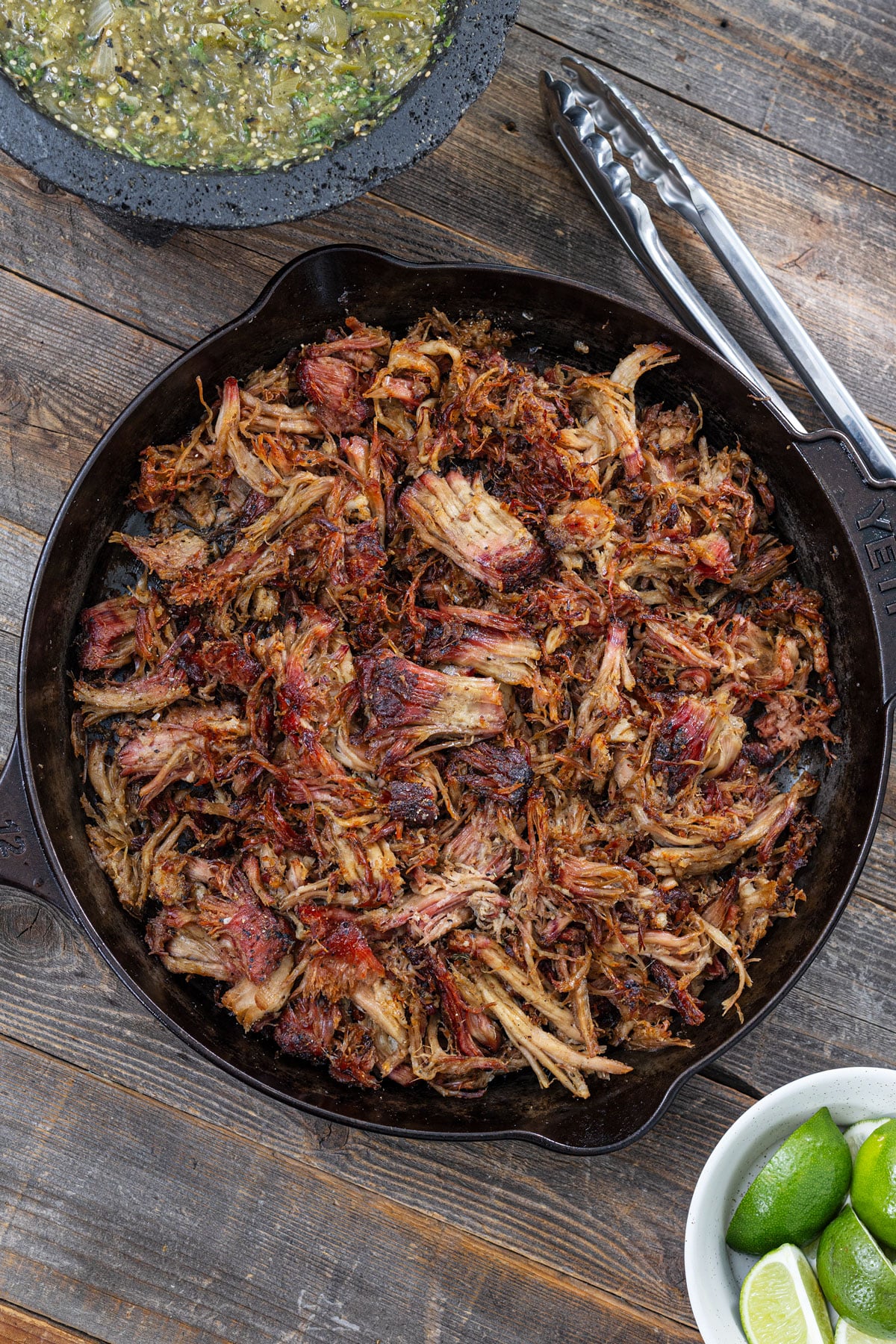 Shredded smoked carnitas crisped in a cast iron skillet with caramelized edges, salsa verde, and fresh limes