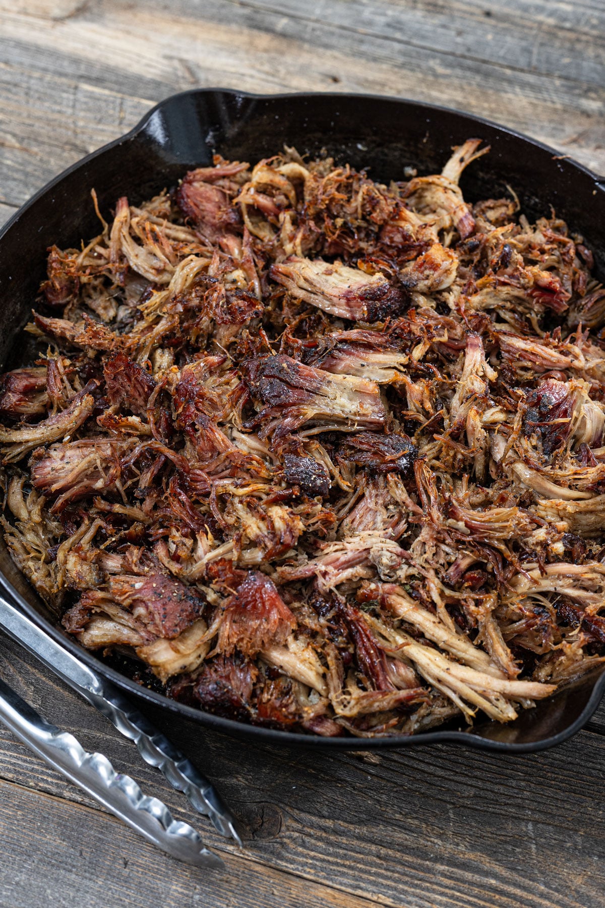Crispy smoked carnitas in a cast iron skillet with caramelized bark pieces throughout