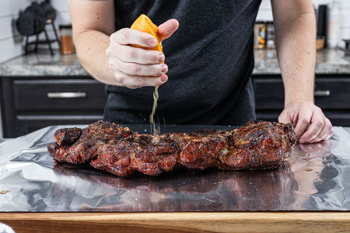 Squeezing fresh orange over smoked pork shoulder before wrapping in foil