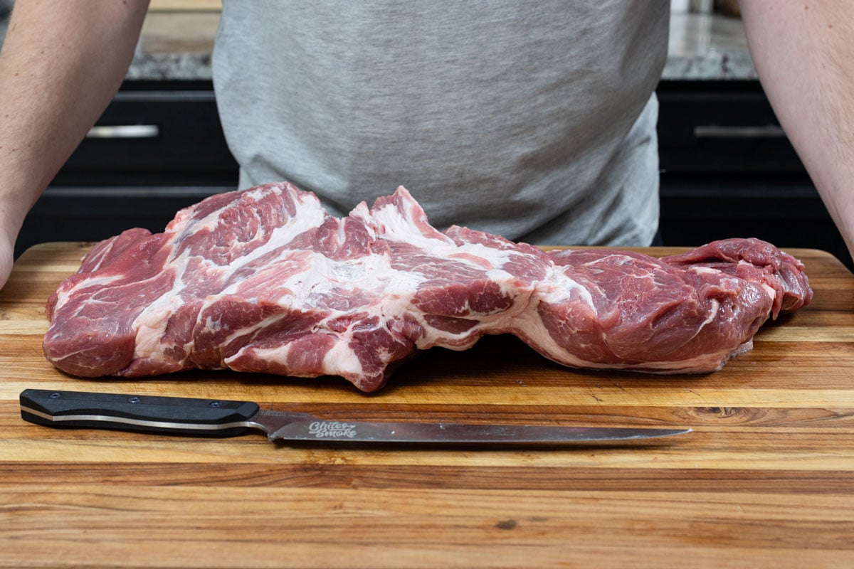 Butterflied pork shoulder laid flat on a wood cutting board with a Chiles and Smoke boning knife