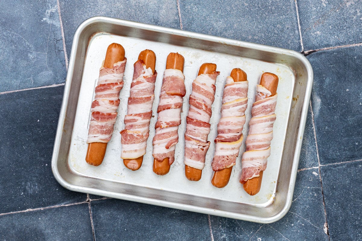 Bacon-wrapped hot dogs on a sheet pan ready to refrigerate before griddling