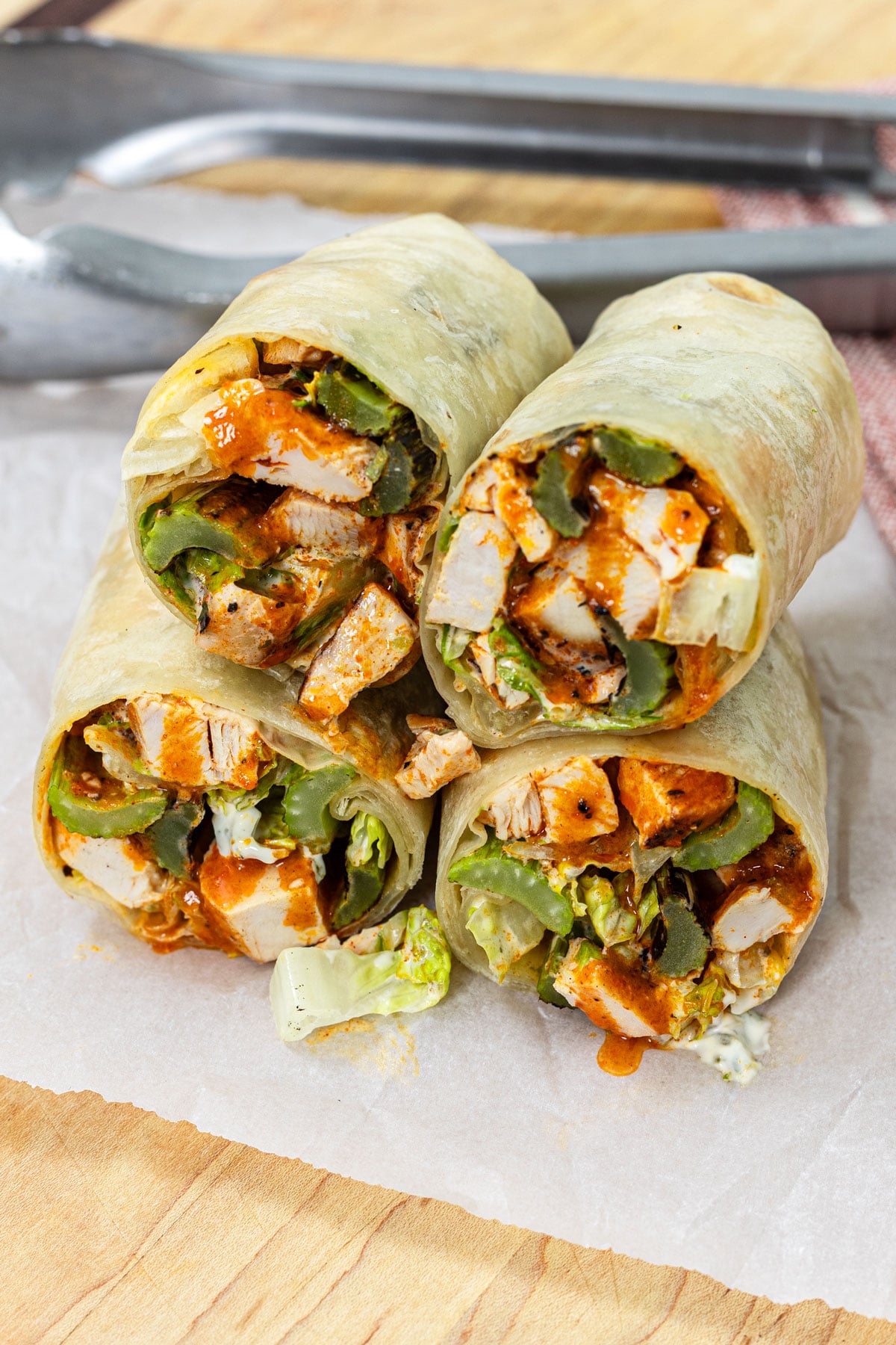 Buffalo chicken wraps sliced and stacked on parchment paper showing grilled chicken, buffalo sauce