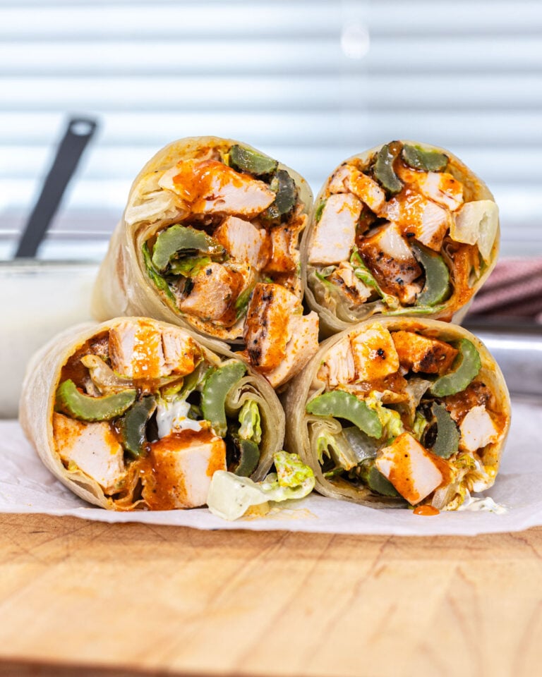 Buffalo chicken wraps sliced and stacked on parchment paper with blue cheese dressing jar in the background