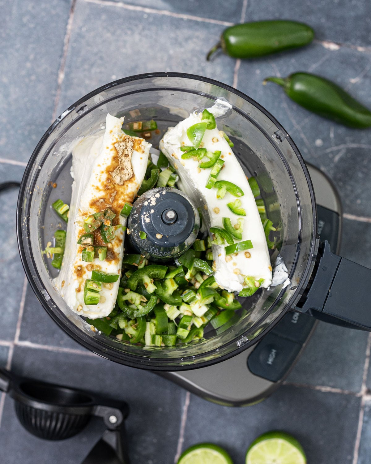 Jalapeño cream cheese ingredients in food processor before blending, cream cheese blocks with diced jalapeños, garlic powder, and lime juice