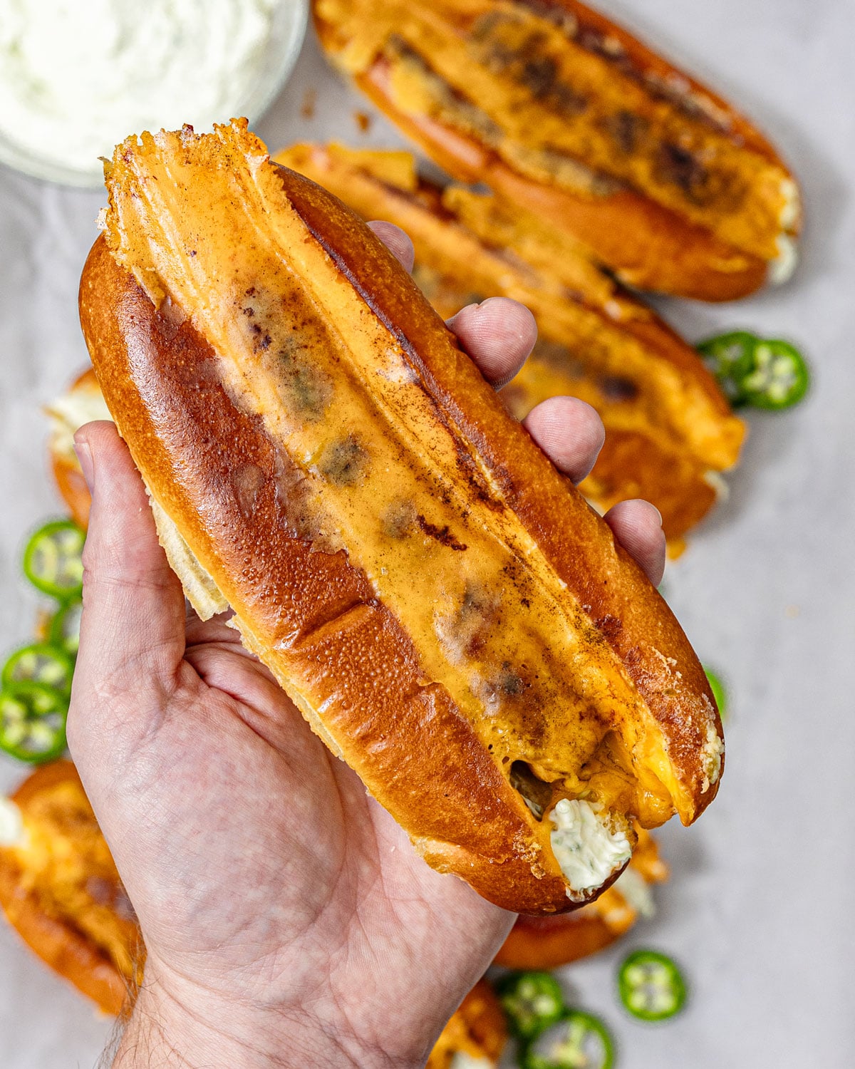 Hand holding a jalapeño popper hot dog showing the seared cheddar crust and jalapeño cream cheese filling
