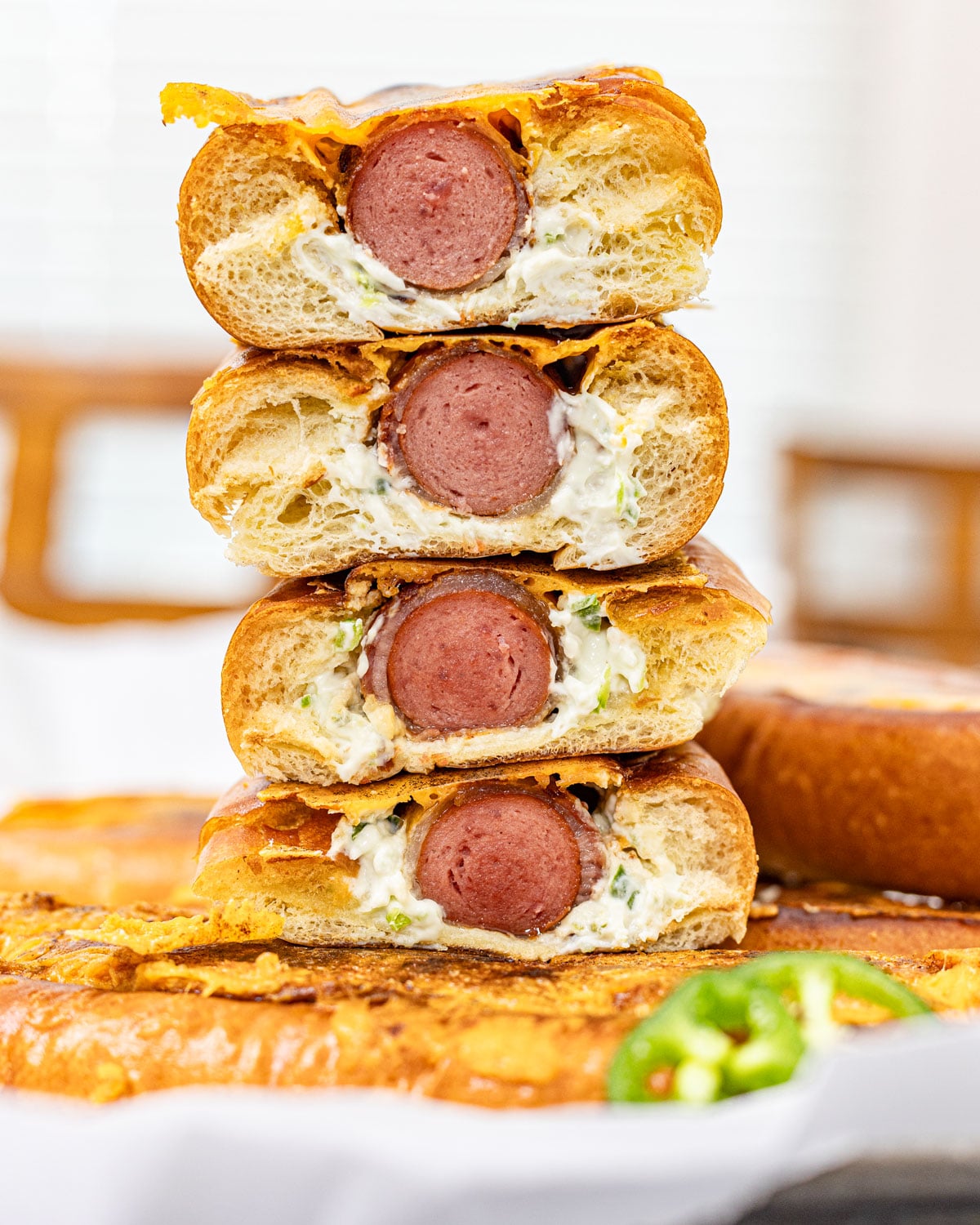 Four jalapeño popper hot dog halves stacked to show the cross-section with bacon-wrapped hot dog, jalapeño cream cheese, and seared cheddar crust