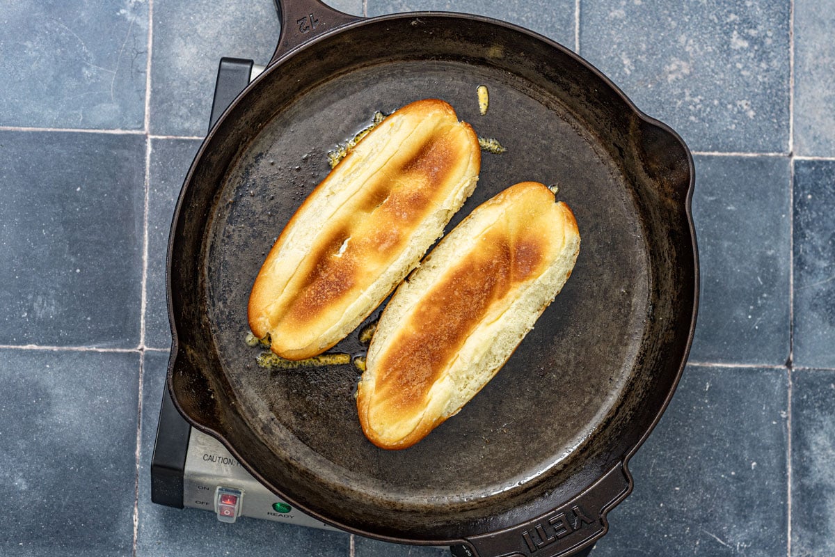 Brioche hot dog buns toasting cut-side down in a buttered cast iron skillet