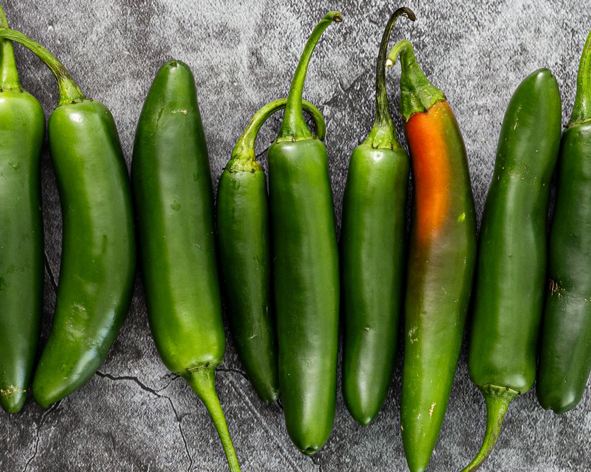 serrano peppers in a row on dark slate, green to red-orange showing the full ripeness range