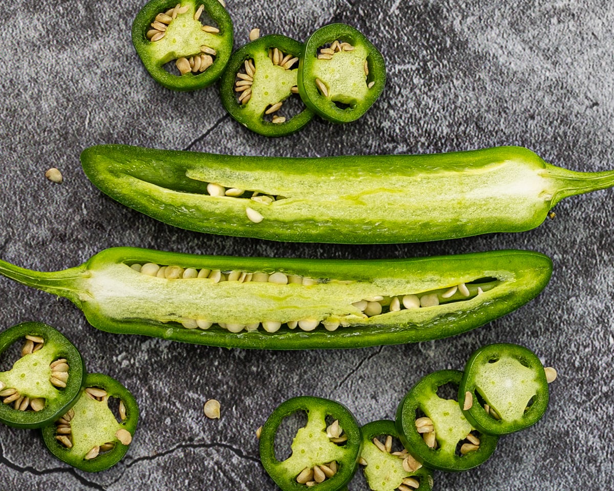 serrano peppers halved lengthwise on dark slate showing seeds and thin walls, with sliced rounds
