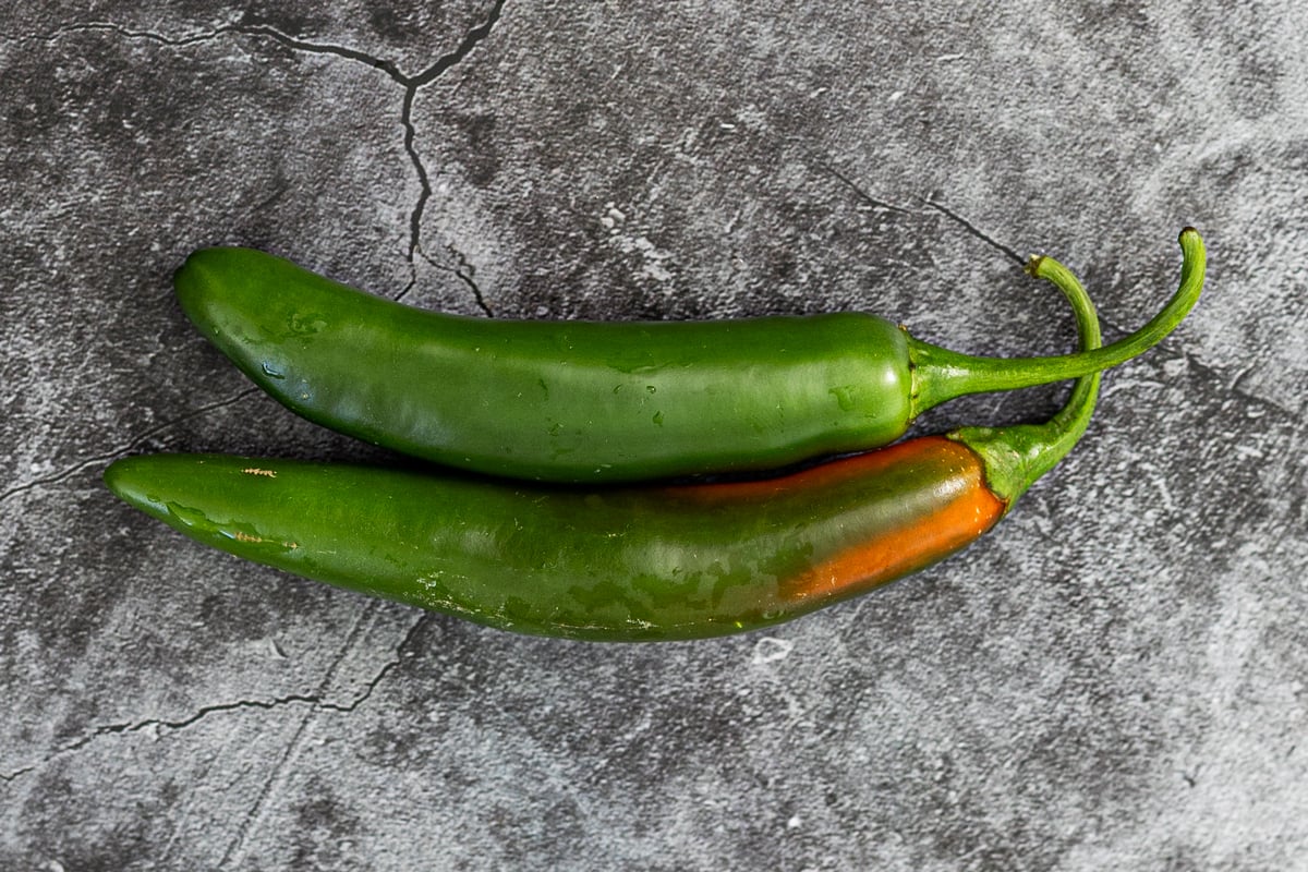 two serrano peppers on dark slate, one green and one beginning to ripen to red-orange