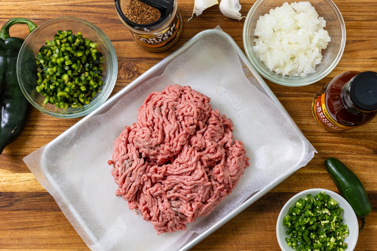 Ingredients for smoked sloppy joes with ground beef, poblano, jalapeño, onion, Canyon Crust, and BBQ sauce on a wood board