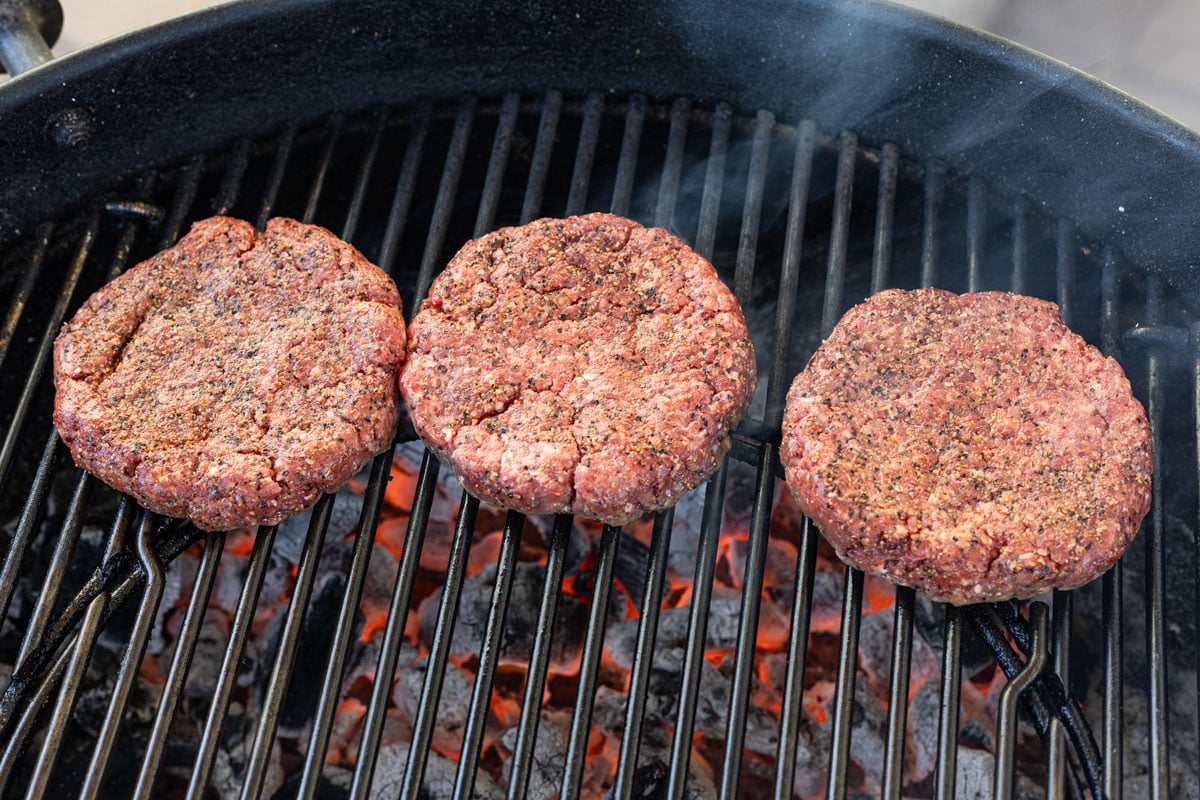 Raw picanha burger patties on a charcoal grill before searing