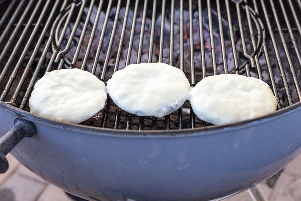 Provolone melting over charcoal-grilled burger patties