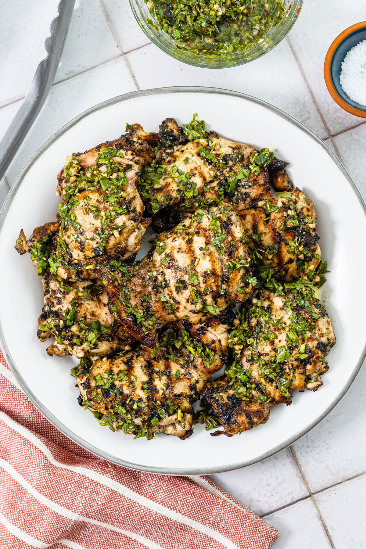 Grilled chimichurri chicken thighs on a plate with fresh chimichurri and flaky salt