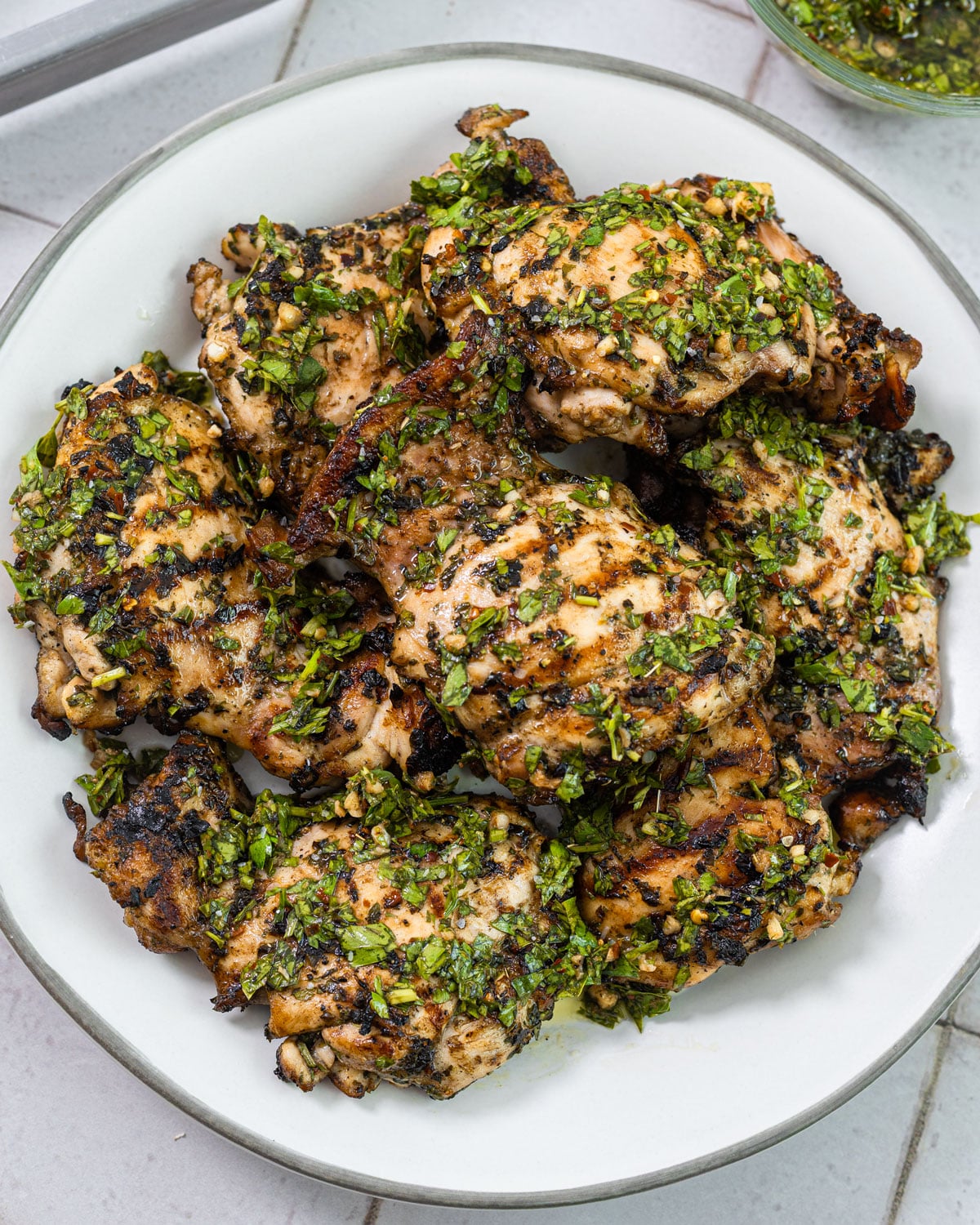 Charcoal-grilled chicken thighs piled on a plate and covered in herby chimichurri
