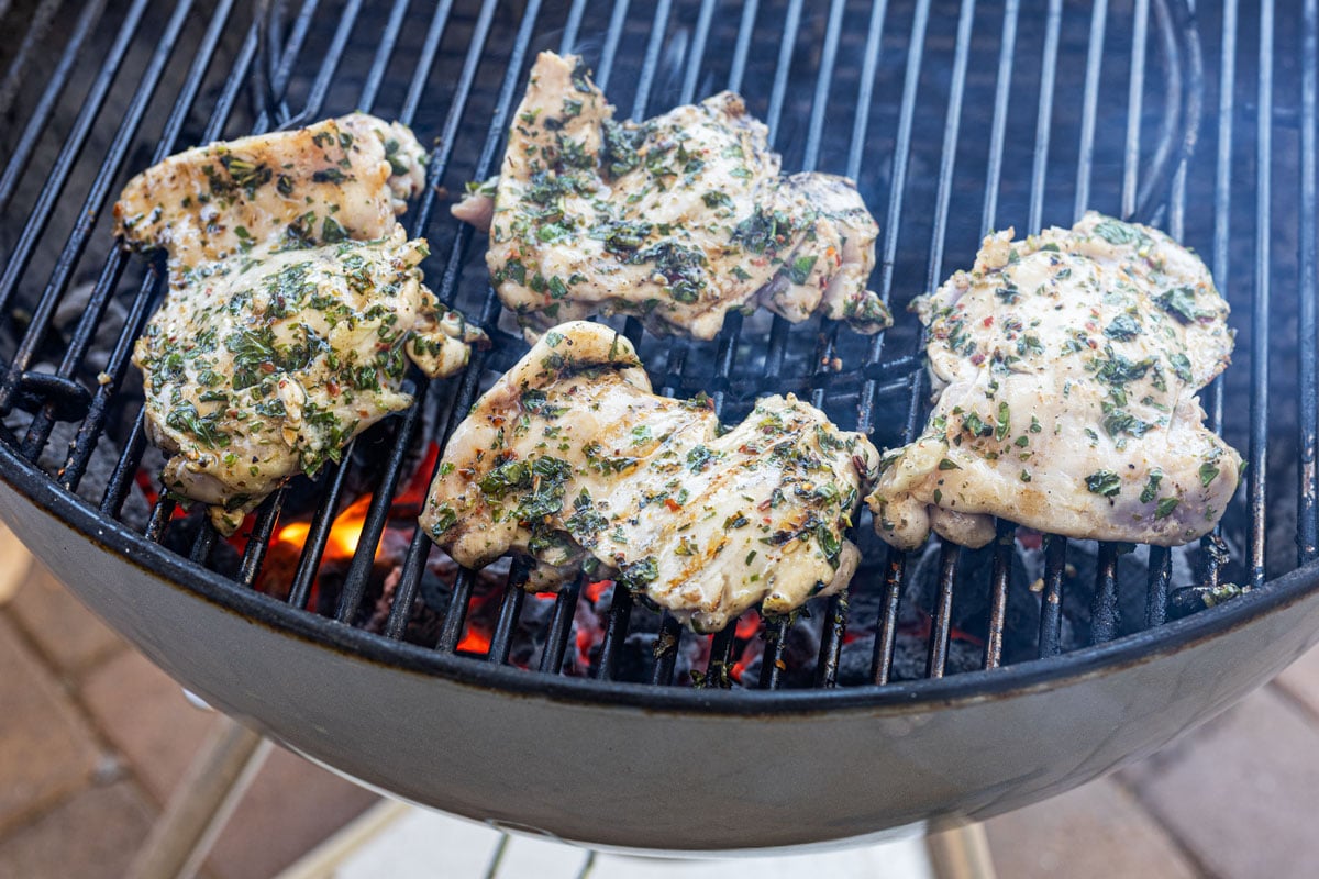 Marinated chicken thighs on a charcoal grill grate over glowing coals