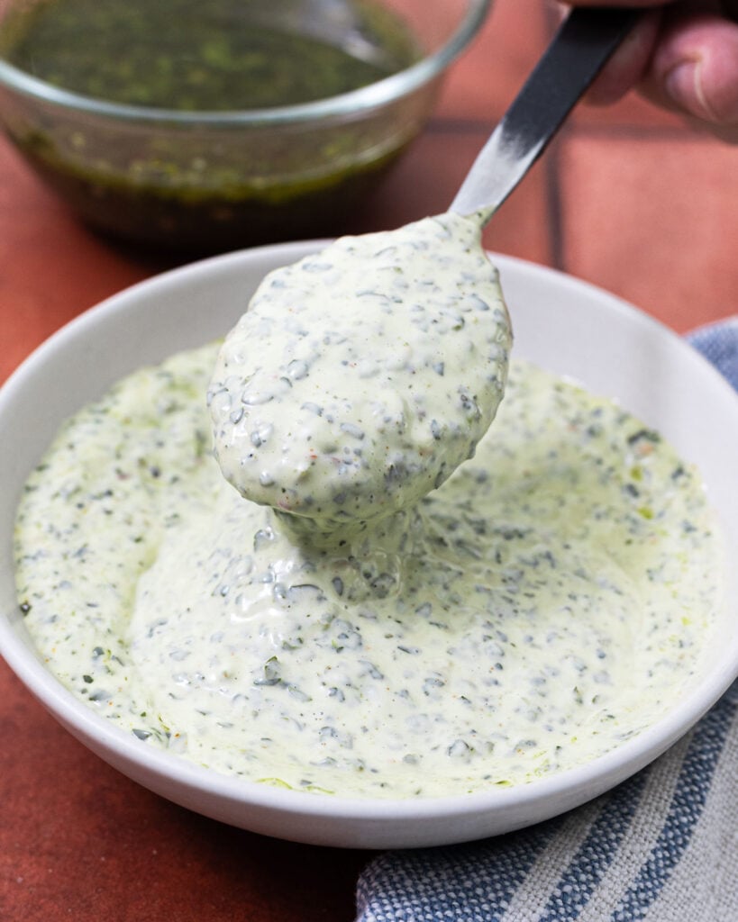 Overhead view of chimichurri mayonnaise in a white bowl with a spoon