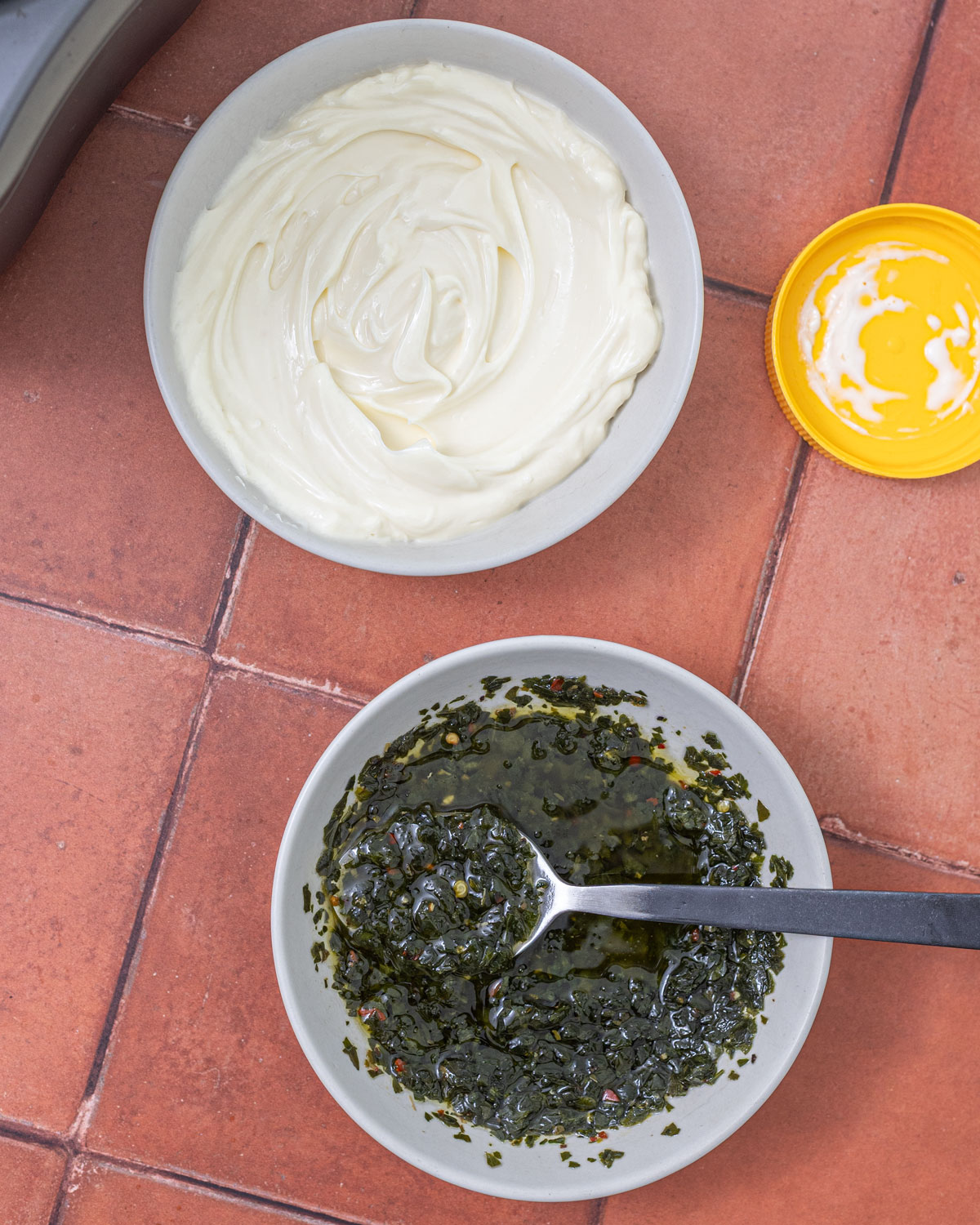 Mayonnaise and drained chimichurri in two white bowls before mixing