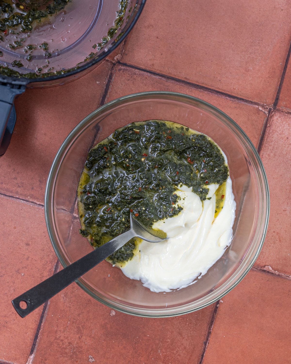 Chimichurri spooned over mayonnaise in a glass bowl, ready to stir together