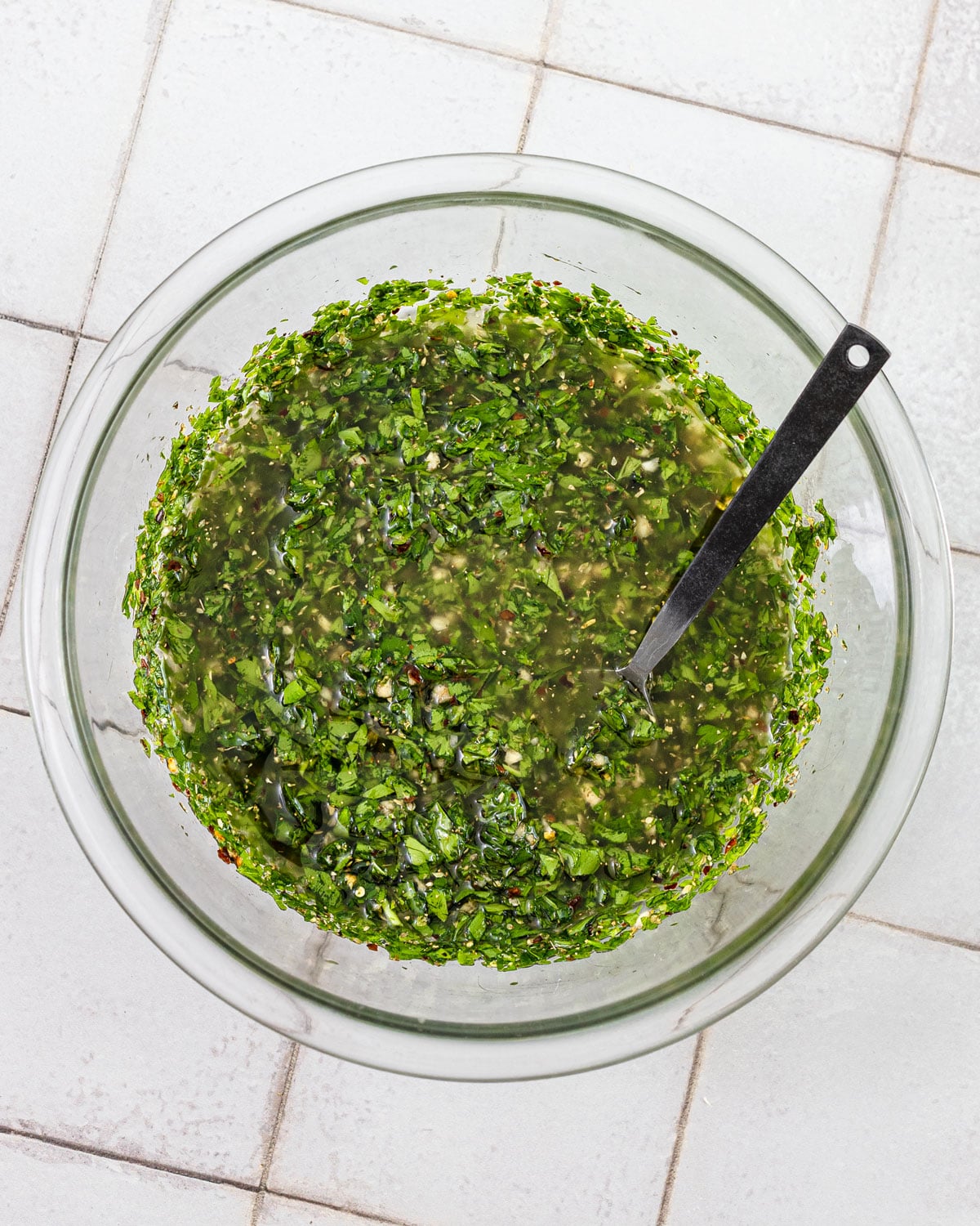 Chimichurri stirred together in a glass bowl with the olive oil mixed in