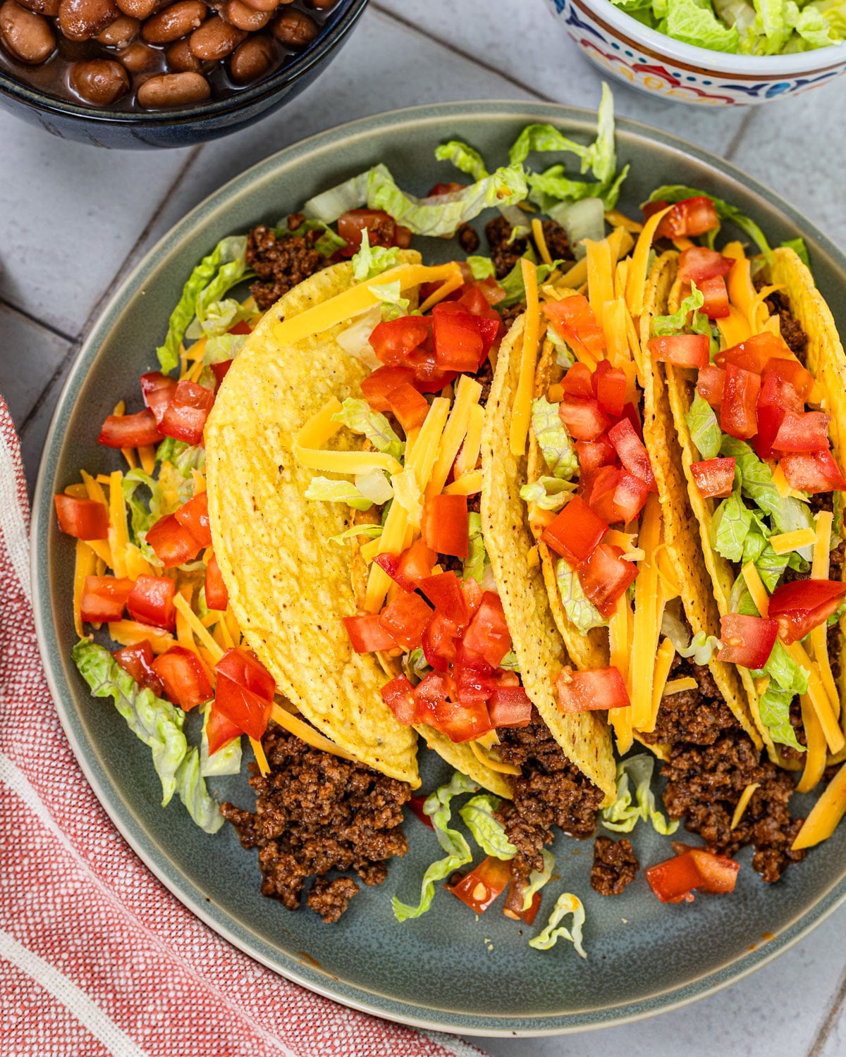 hard shell tacos filled with seasoned ground beef, shredded lettuce, cheddar cheese, and diced tomatoes on a plate