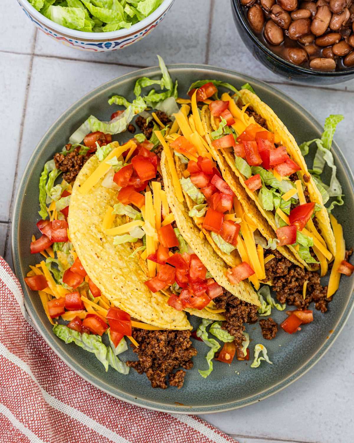 overhead hard shell tacos with seasoned ground beef, shredded lettuce, cheddar, and diced tomatoes on a plate