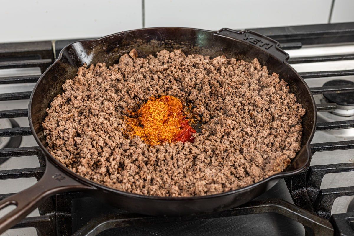 seasoning and tomato paste added to center of browned ground beef in a cast iron skillet